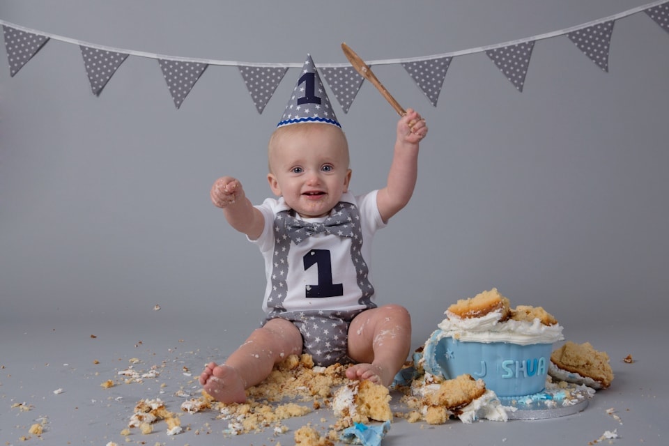 One year old boy wearing a top and hat with the number 1 on it smashing cake for his baby cake smash photography session