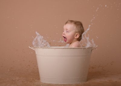 Baby boy splashing in bath for first birthday cake smash in Northampton
