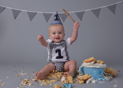 One year old boy wearing a top and hat with the number 1 on it smashing cake for his baby cake smash photography session