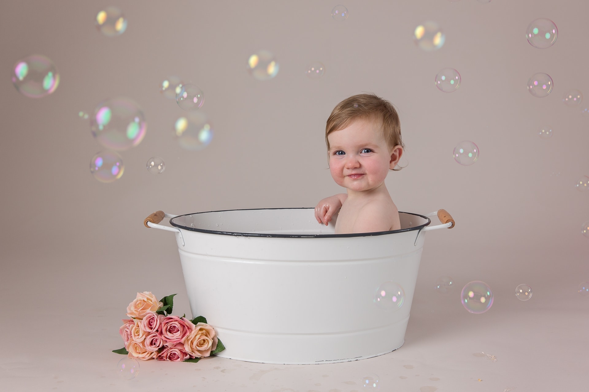 Baby girl in tub with bubbles and flowers on the floor for first birthday cake smash photography session