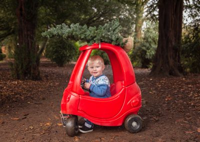 Young boy sitting in red little tykes car with Christmas Tree on the top