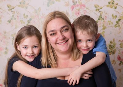 Mother and two children all smiling at camera with floral background