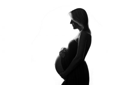 Silhouette of maternity photography session of mum holding her bump looking to the left