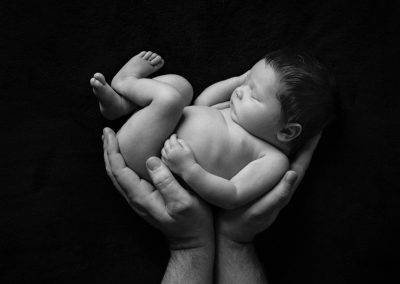 Baby girl held by dads hands on black background for newborn photoshoot in Northampton
