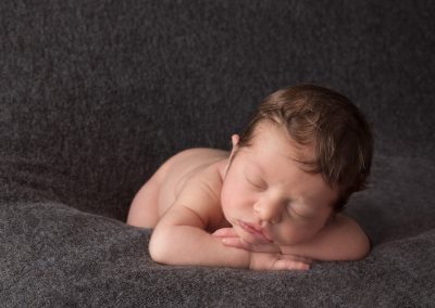 Baby boy asleep head on hands on grey background for newborn photoshoot in Northampton