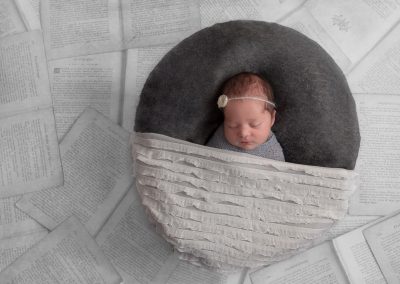 Baby girl in grey round basket on pages of books
