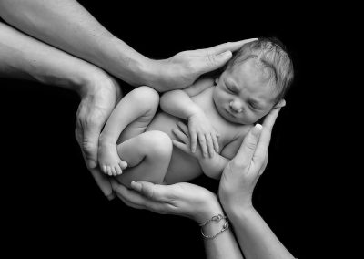 Baby girl held by parents hands on black background for newborn photoshoot in Northampton