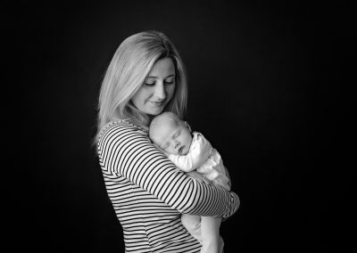 Baby girl being held by mother in stripe top on black background for newborn photography session in Northampton