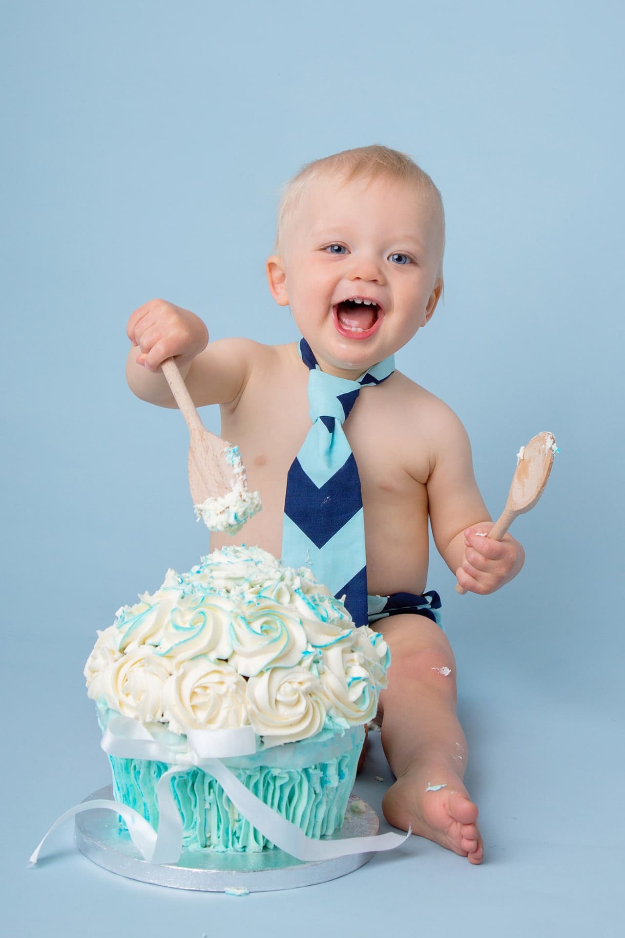 Baby cake smash with boy laughing in front of blue cake