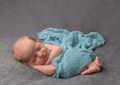 Baby girl in green wrap on grey background