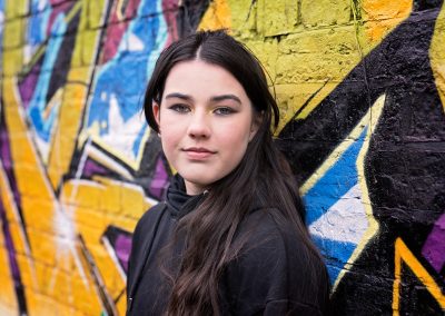 Girl with long dark hair leaning against graffiti wall