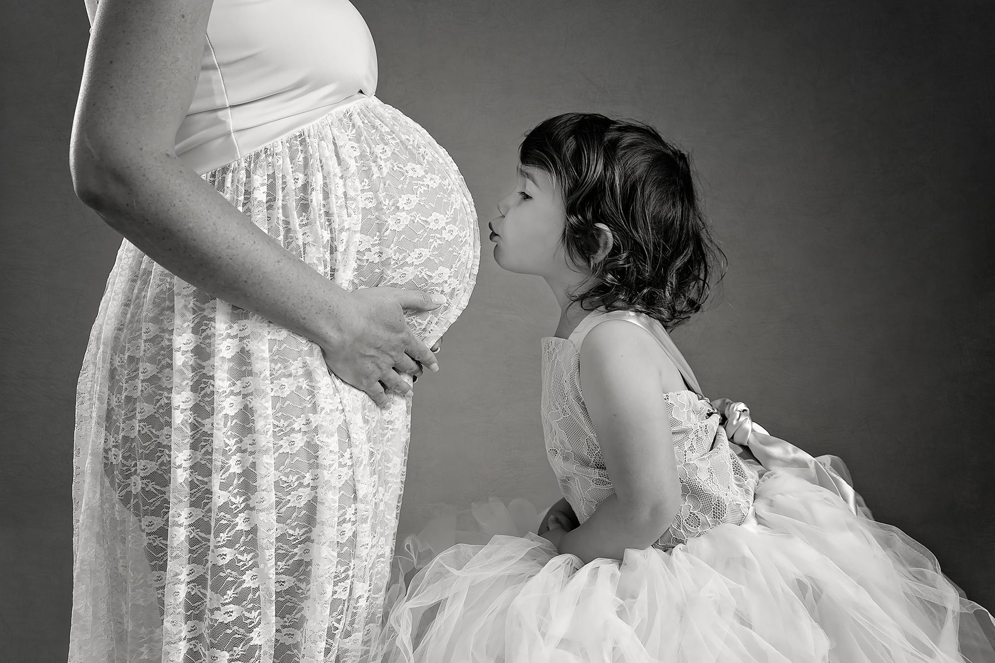 Maternity photograph of pregnant lady with young girl kissing her bump in Northamptonshire