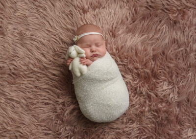 newborn baby girl on a pink blanket, in a white wrap and headband