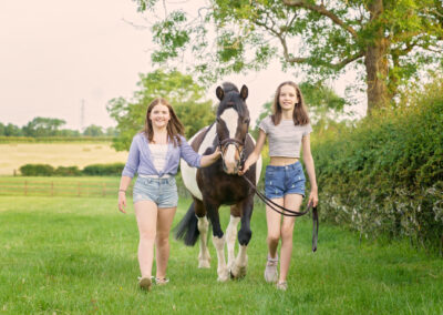 two teenage girls leading coloured pony through the field in Northamptonshire