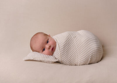 awake newborn baby lying on cream blanket