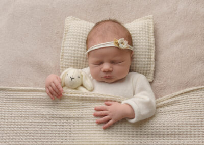 newborn baby lying in bed cuddling toy rabbit